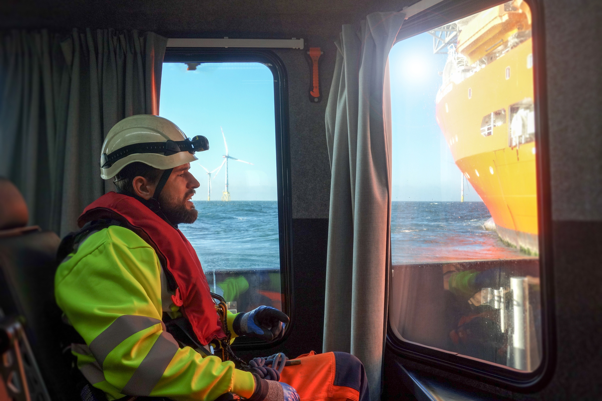 Offshore manual worker sitting in transfer vessel by window and looking out